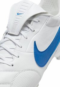 Botas de fútbol blancas con un upper de cuero suave, logo de swoosh azul, acentos perforados texturizados y cordones blancos; incluye una solapa de soporte para el tobillo.