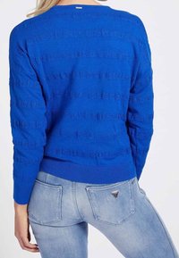 Suéter de punto azul con un patrón texturizado, escote redondo y dobladillo acanalado. Combinado con pantalones vaqueros azul claro que incluyen bolsillos traseros y un detalle de logo.