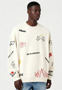 Sudadera crema con diversos diseños bordados: corazones, flores, serpientes, texto y llamas. Corte holgado con puños acanalados.