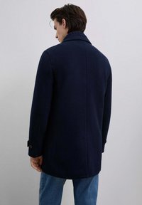 Marineblå uldfrakke med notch-krave, to knapper på hver ærme og en skræddersyet pasform, parret med lyseblå jeans.