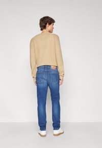 Beige stickad tröja med ribbad textur, kombinerad med blå tapered jeans som har bakfickor och en märkesetikett. Vita sneakers fulländar looken.