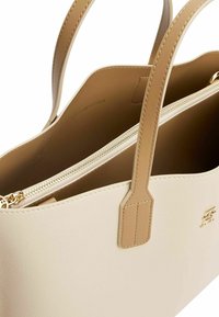 Beżowa skórzana torba na ramię z podwójnymi uchwytami, złotym zamkiem błyskawicznym i subtelnym logo. Gładka faktura z przestronnym wnętrzem.