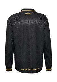 Fekete hosszú ujjú sportdzseki finom cseppmintázattal, sárga "hummel" logóval a nyakon, és "INTERNATIONALS" felirattal az alján.