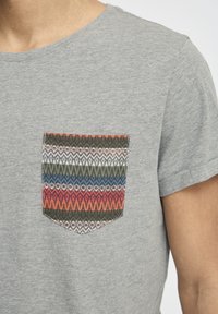Grå bomull T-skjorte med en flerfarget mønstrete lomme med geometriske design i rød, blå, grønn og beige. Korte ermer.