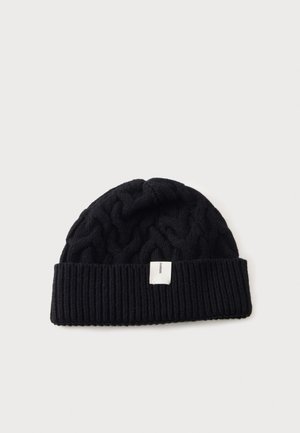 Black knitted beanie with a folded ribbed brim and a small white rectangular label on the front center.