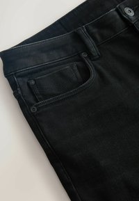 Melnas denima bikses ar klasisku piecu kabatu dizainu, diskrētu šuvju un vidēju vidukli ar gludu faktūru.