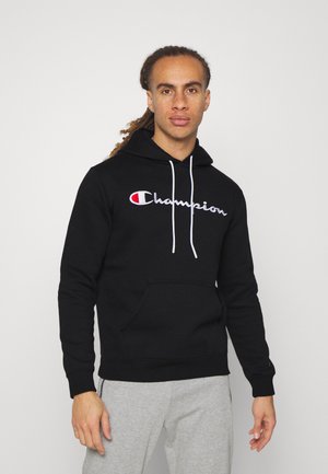 Sudadera negra de algodón, con cordones blancos y logotipo bordado de "Champion". Bolsillo tipo canguro en la parte delantera, así como puños y dobladillo acanalados.