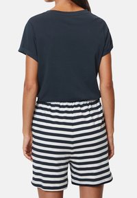 Kvinna som bär en marinblå kortärmad topp och högmidjade svartvita horisontella randiga shorts, sedd bakifrån.