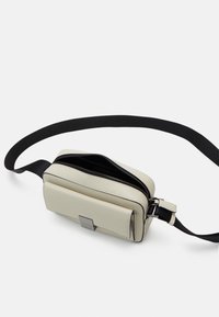 Lichtbeige leren schoudertas met een zwarte verstelbare schouderriem, een klepzak aan de voorkant en een gedeeltelijk open hoofdritscompartiment.