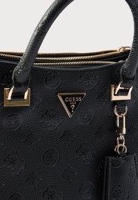 Czarna torebka o fakturze z wytłoczonym wzorem logo, złote okucia, podwójne zamknięcie na zamek oraz odpinana zawieszka przymocowana do paska.