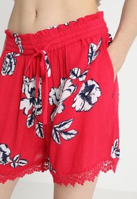 Rode bloemen short van lichtgewicht stof, met een rimpel tailleband, striksluiting en kantafwerking aan de onderkant.