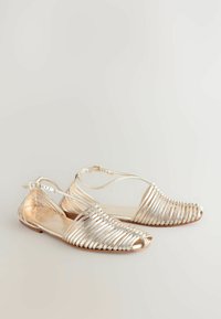 Metallilised kuldsed sandaalid horisontaalsete ja vertikaalsete riba mustriga, avatud varbaga, säärepaelaga, lamedal tallal ning ees koormatud kudumiga.