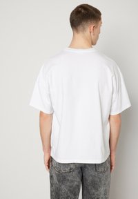 Balta kokvilnas t-krekls ar brīvu piegriezumu, īsām piedurknēm un izliekto apakšmalu. Valkāts kopā ar pelēkiem, nolietotiem džinsiem. Vienkāršs, universāls dizains.