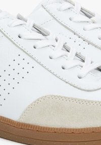 Białe skórzane sneakersy z szarymi zamszowymi akcentami, okrągłym noskiem, perforowanym wzorem dla lepszej wentylacji oraz gumową podeszwą.