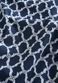 Țesătură marină cu un model geometric alb texturat, având un design matlasat. Materialul pare moale, cu accente distincte pe tot parcursul său.