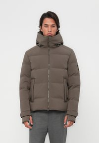 Polstret jakke i en dæmpet brun farve med h�øj krave, lynlås lukning, sidelommer og ribkantede ærmer. Stoffet ser glat og holdbart ud.