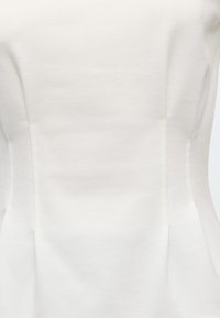 Gros plan d’un vêtement blanc ajusté montrant des coutures structurées et une texture de tissu lisse.