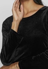 Top de terciopelo negro de manga larga con cuello redondo y tejido texturizado, que muestra un brillo distintivo y costuras suavemente acabadas.