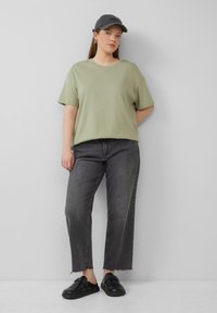 Olijfgroen katoenen t-shirt, relaxte pasvorm, gecombineerd met high-waisted, donkergrijze denim jeans. Zwarte instap schoenen en een donkere pet maken de outfit compleet.