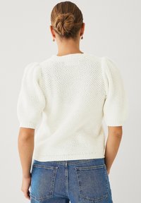 Maglione bianco lavorato a maglia con maniche corte a palloncino, caratterizzato da un motivo testurizzato e orlo a costine, abbinato a jeans blu a vita alta.