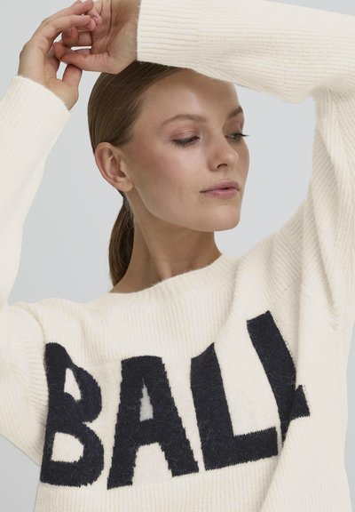Un pull en tricot de couleur crème avec un grand graphique "BALL" bleu marine. Le design comprend une texture côtelée et une encolure large.