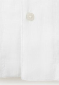 Poignet de chemise en lin blanc avec un seul bouton blanc et un détail de couture visible le long du bord.