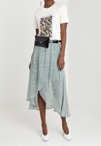 Wit t-shirt met bloemenprint, gecombineerd met een asymmetrische rok in muntgroen met bloemenpatroon. Zwarte heuptas en witte hakken.