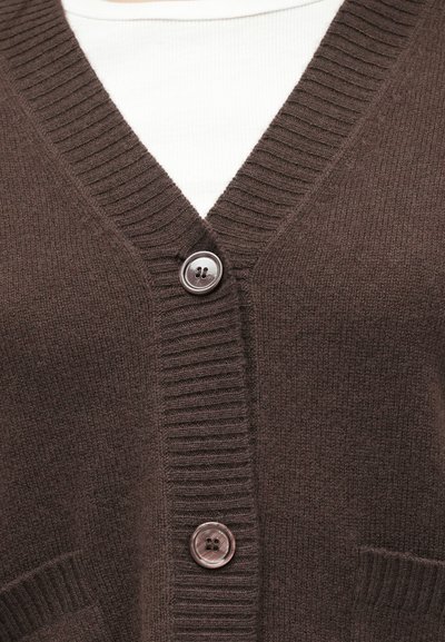Rjava pletena jopica z V-izrezom, robovi s rebrastim vzorcem, dvema sprednjima žepoma in srebrnim gumbom na prsnem delu.