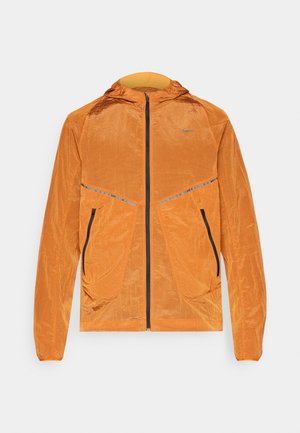 Chaqueta naranja de Nike con capucha, tejido texturizado, cierre completo, dos bolsillos frontales con cremalleras negras y detalles reflectantes.