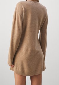 Brązowa dzianinowa sukienka swetrowa z długimi rękawami, luźnym krojem i ściągaczem. Miękka struktura i minimalistyczny design, bez widocznych wzorów czy akcentów.