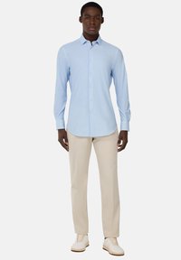 Camisa de botones azul claro con mangas largas, combinada con pantalones beige y zapatillas blancas. La camisa presenta un cuello clásico y una textura sutil.