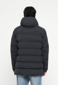 Dark gray puffer jacket with a high collar, featuring a quilted design and stitched panels, paired with light blue jeans.
