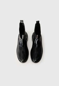 Botas Chelsea negras de goma con un acabado liso y brillante, altura hasta el tobillo, tiradores en el bucle y una suela duradera con un ligero tacón.