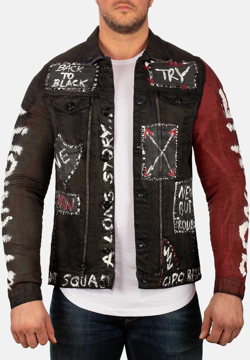 Veste en denim noir avec des manches rouges, présentant des textes et des motifs en blanc et rouge. Des détails cloutés mettent en valeur les poches et les bordures.