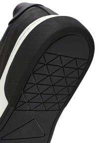 Suola di scarpa in gomma nera con un motivo texturizzato per la presa e un accento bianco lungo il bordo, caratterizzata da un design triangolare su un lato.