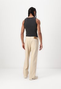 A gray ribbed tank top paired with cream-colored, pinstriped wide-leg pants, featuring a logo patch near the back pocket.