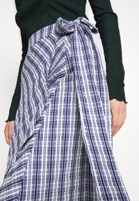 Blå och vit rutigt kjol med en knuten rosett i midjan, med en texturerad finish och inslagdesign. Materialet verkar lätt och flödande.