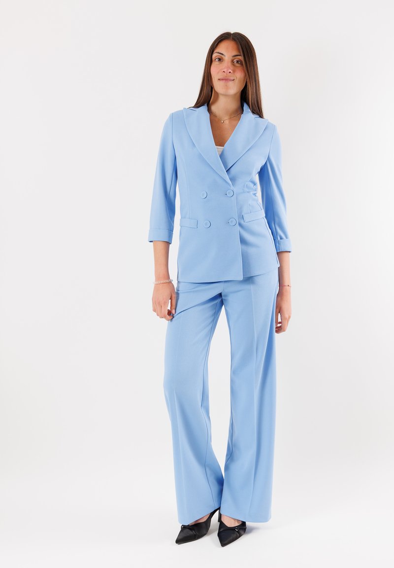 Blazer su misura azzurro chiaro e pantaloni a gamba larga, con design doppiopetto, rever a risvolto e tessuto morbido. Scarpa nera a punta.