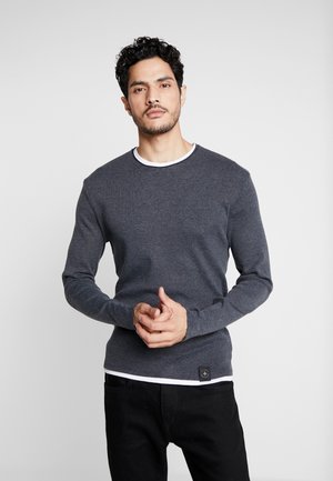 Graues Langarmshirt mit weißem Rundhalsausschnitt, aus einem strukturierten Stoff gefertigt, mit einem kleinen Logo-Patch am Saum.
