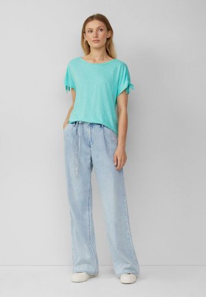 Licht turquoise kortekorte mouwen shirt met knoopaccenten, gecombineerd met lichtblauwe hoge taille brede jeans, gedragen met witte canvas schoenen.
