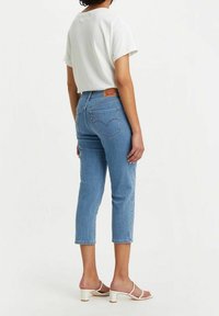 Jeans de denim azul claro con corte tapered y puños enrollados, combinados con una camisa blanca de manga corta y sandalias de tacón cuadrado color crema.