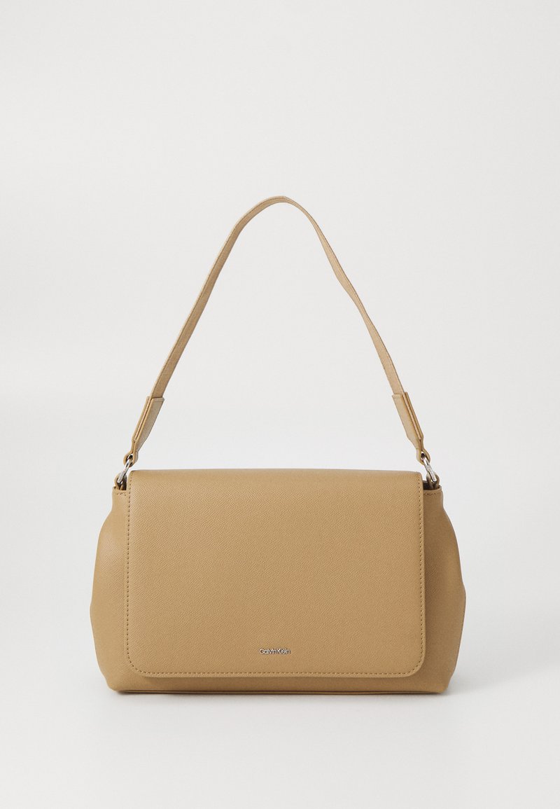 Sac à main en cuir synthétique tan avec une fermeture à rabat, une bandoulière unique et un logo de marque en argent à l'avant. Texture lisse.