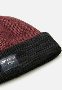 Strikket hue med en maroon top og en struktureret sort manchet. Har et syet logo-patch på manchetten. Blødt materiale med et ribbet design.