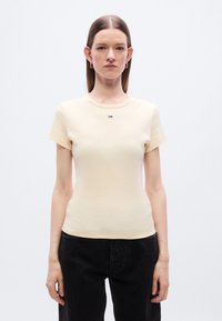 Φωτεινό κίτρινο εφαρμοστό μπλουζάκι με κοντά μανίκια, στρογγυλή λαιμόκοψη και μικρό λογότυπο στο στήθος. Βαμβακερό υλικό με ομαλή υφή.