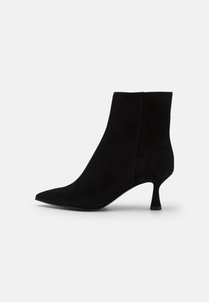 Czarny zamszowy botek na kostkę z zaostrzonym noskiem, średniej wysokości zakrzywionym obcasem i gładką cholewką, pokazany z profilu na białym tle.