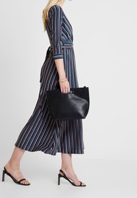 Robe rayée en bleu, blanc et orange, avec des manches trois-quarts et une taille nouée, accompagnée d'un sac à main en cuir noir et de sandales à talons noires.