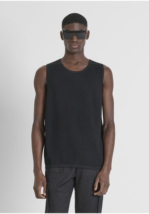 Top negro de canalé sin mangas con cuello redondo, combinado con pantalones negros. La tela tiene un patrón texturizado, creando un look estratificado.