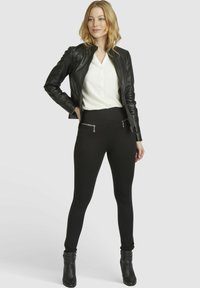 Black faux leather jacket, white button-up shirt, black high-waisted leggings with zippers, and black ankle boots. Smooth texture, fitted design.