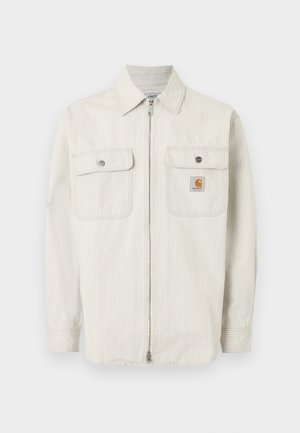 helebeežist beige tõmblukuga jakk peenikeste vertikaalsete triipudega, kahe nööbitava rinnataskuga ja väikese Carhartti logoga paremal taskul.