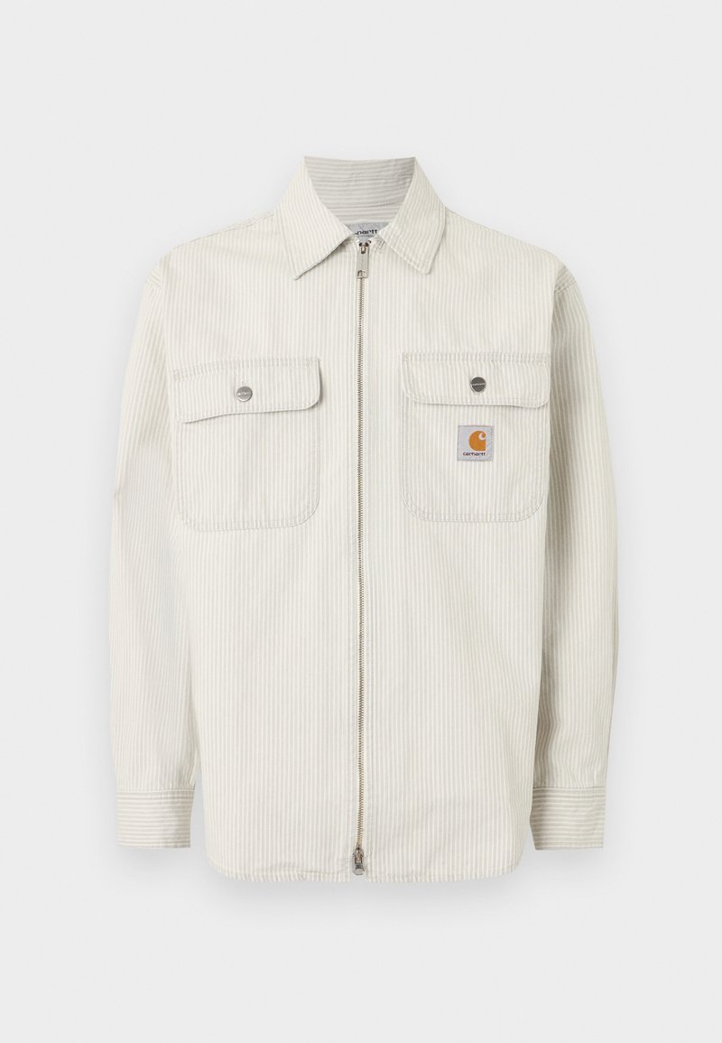 Hellbeige Jacke zum Hochziehen mit feinen vertikalen Streifen, zwei Brusttaschen mit Knöpfen und einem kleinen Carhartt-Logo auf der rechten Tasche.